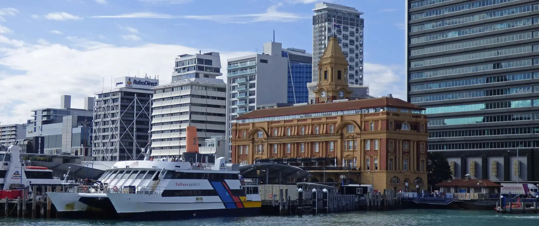 Frente ao porto com balsa, edifício histórico e arranha-céus altos ao fundo em Auckland, Nova Zelândia.