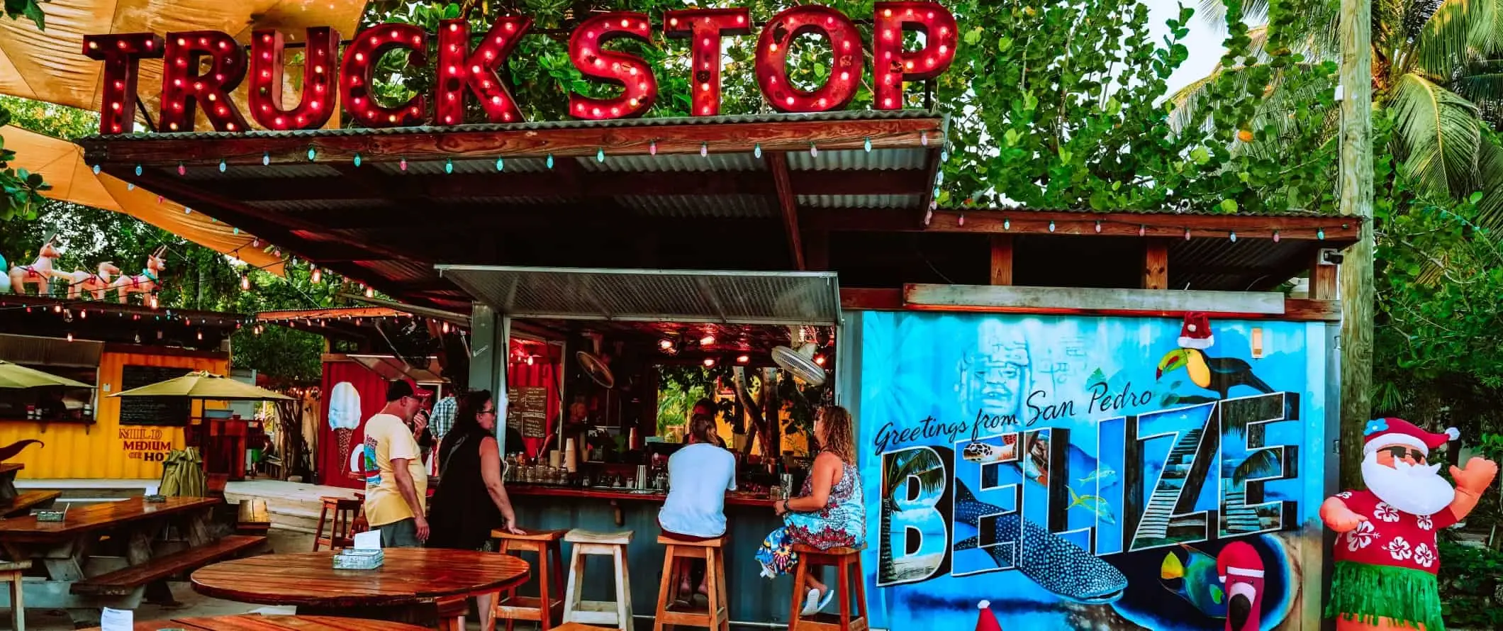 Gente sentada en un bar de playa con un enorme cartel de neón que dice