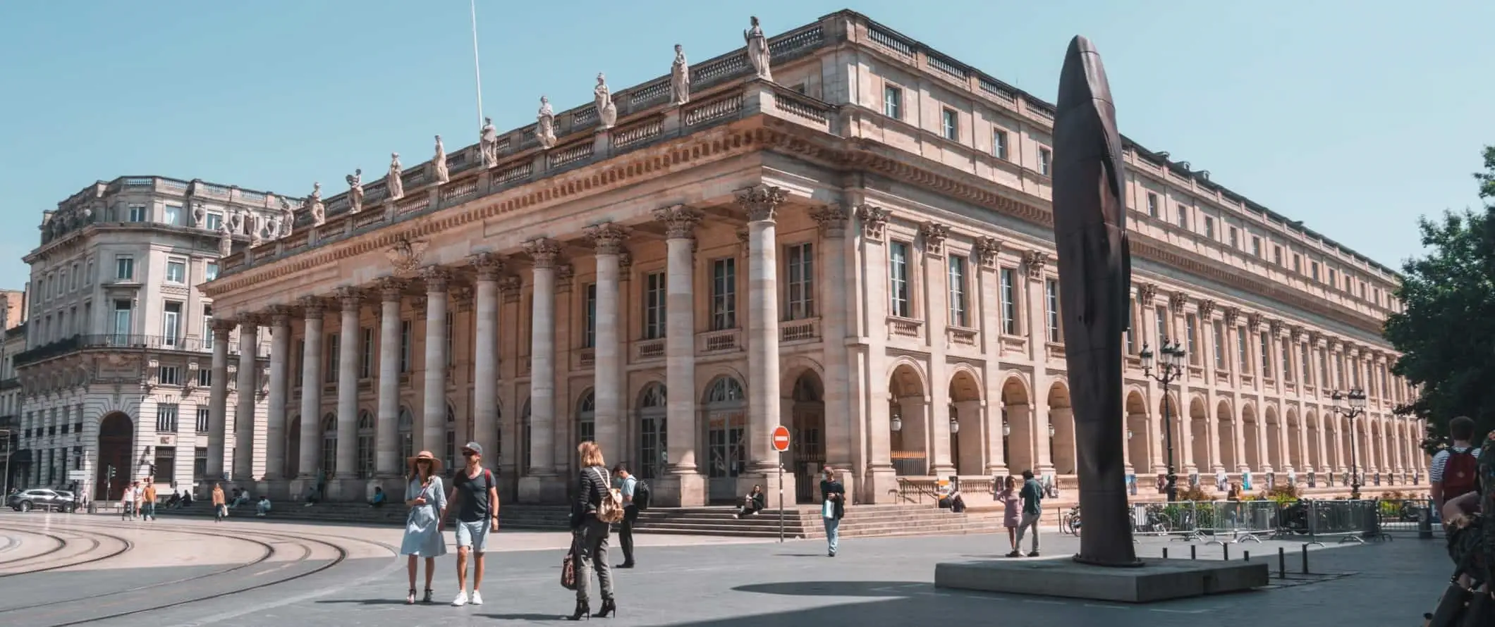 Menschen, die über einen Platz vor einem großen Säulengebäude in der Altstadt von Bordeaux, Frankreich, gehen