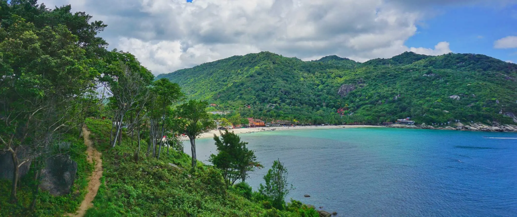 Een wandelpad door het weelderige bos met een turquoise baai op de achtergrond op het eiland Ko Pha Ngan, Thailand bij zonsondergang boven de oceaan