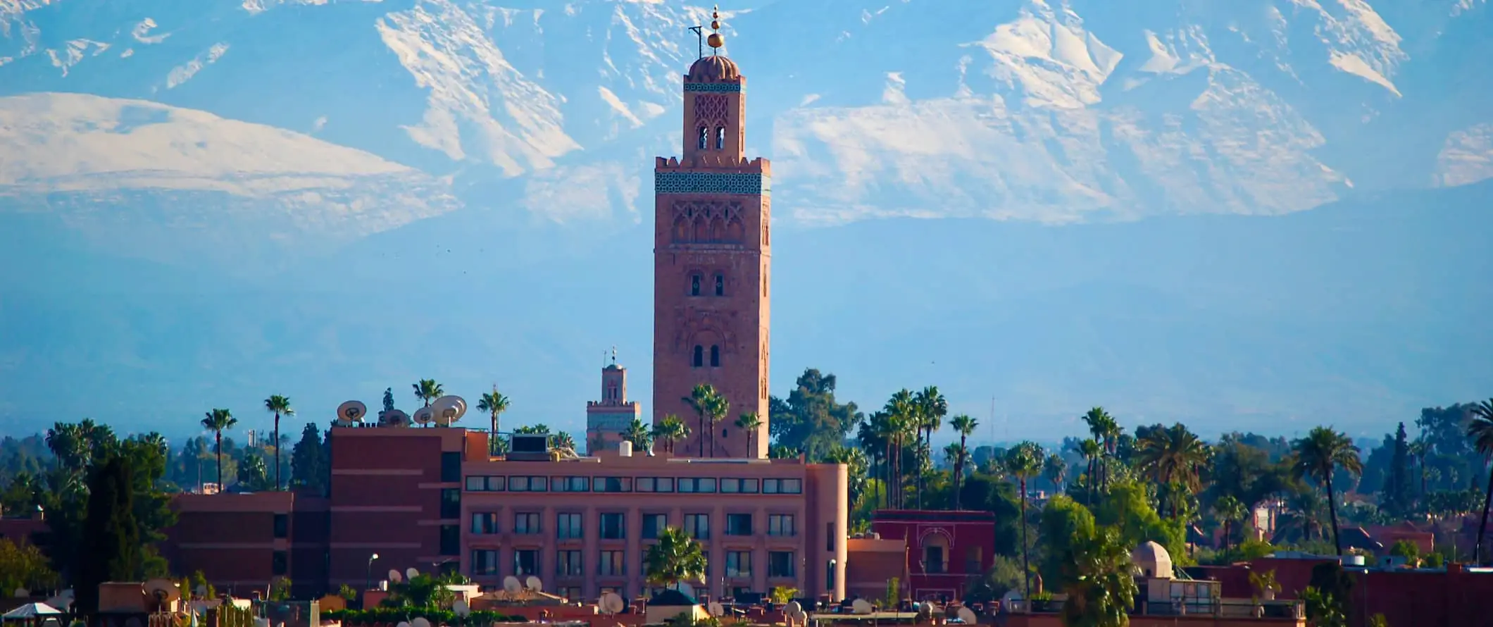 Stadtansicht von Marrakesch, Marokko mit einem Turm im Vordergrund und atemberaubenden Bergen in der Ferne