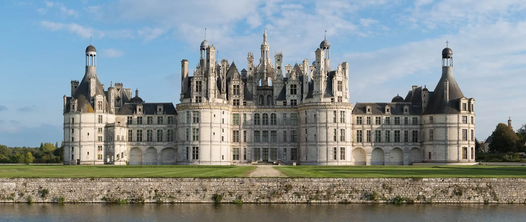 Um enorme castelo histórico francês no Vale do Loire, cercado por grama e vegetação