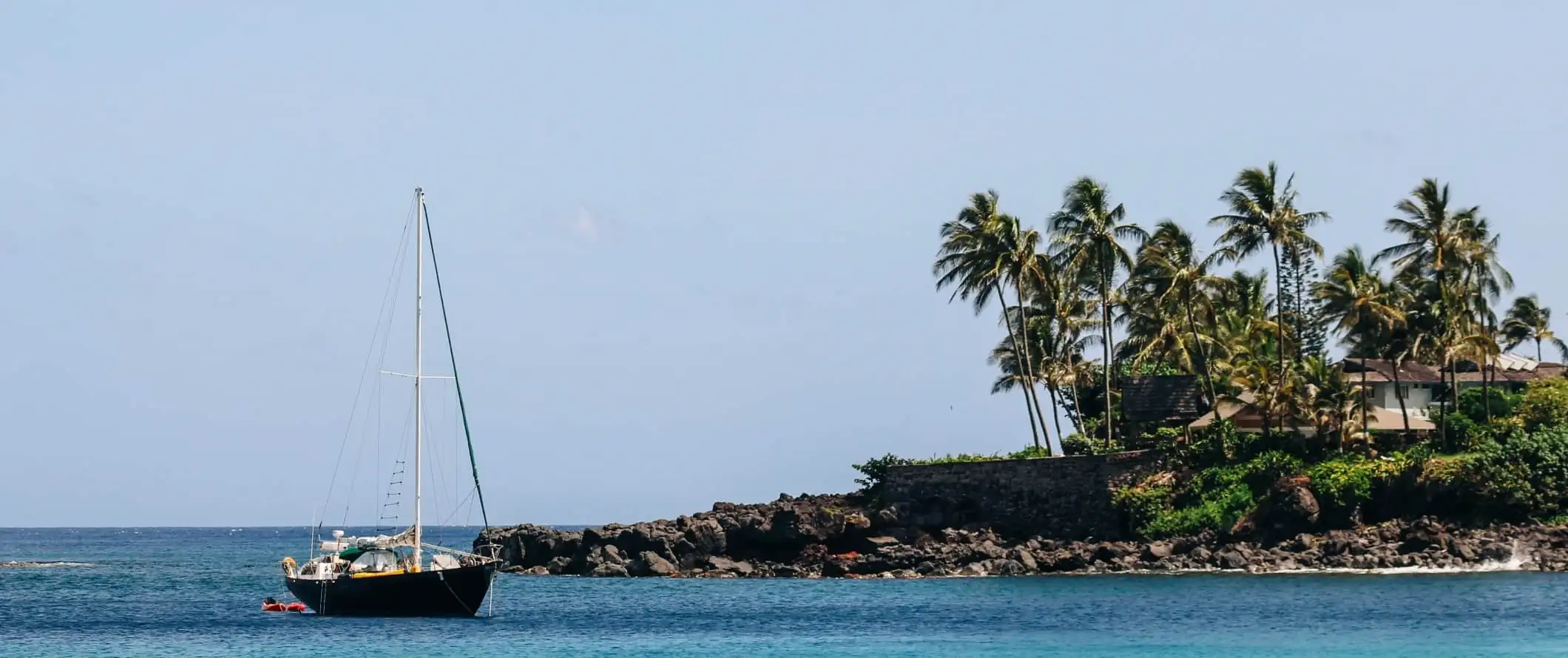 Isang sailboat na lumulutang sa isang daungan na may mga puno ng palma sa baybayin sa labas ng Caribbean na isla ng Saint Lucia