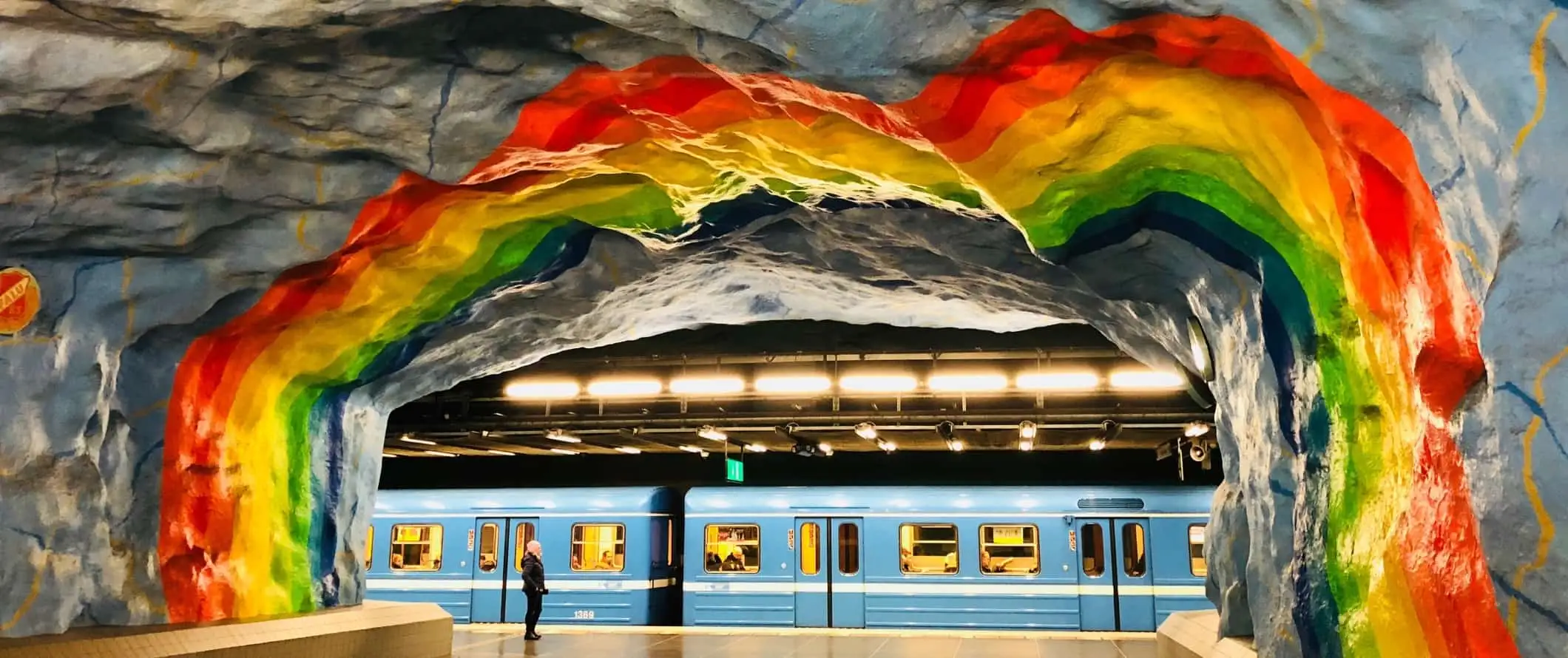 Een regenboogmuurschildering in de metro met een blauwe trein die het station van Stockholm, Zweden binnenrijdt