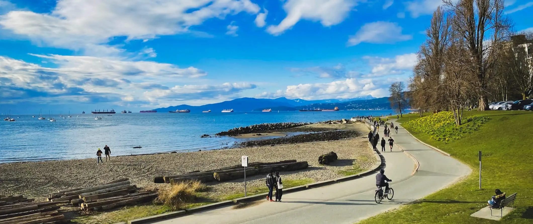 Lidí, kteří jdou a jezdí na kole podél pobřeží slunného Vancouveru, Kanada