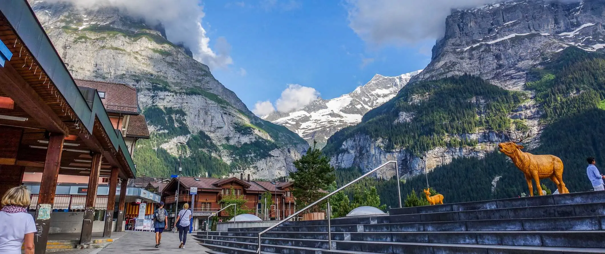 Menschen, die in Interlaken, Schweiz, durch eine Straße zwischen Holzchalets laufen und im Hintergrund dramatische Berge aufragen