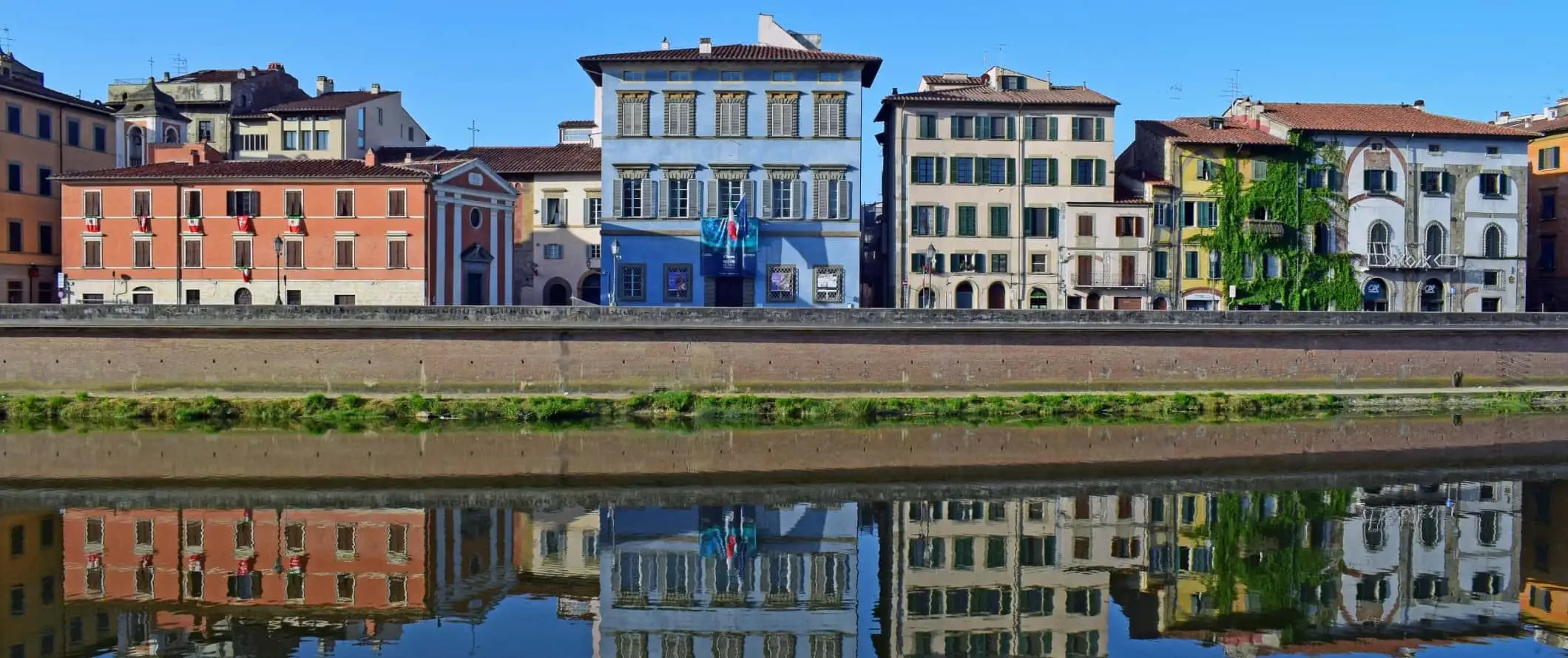 Bangunan bersejarah berwarna cerah, termasuk pusat seni berwarna biru, Palazzo Blu, di sepanjang tepi Sungai Arno di Pisa, Italia.