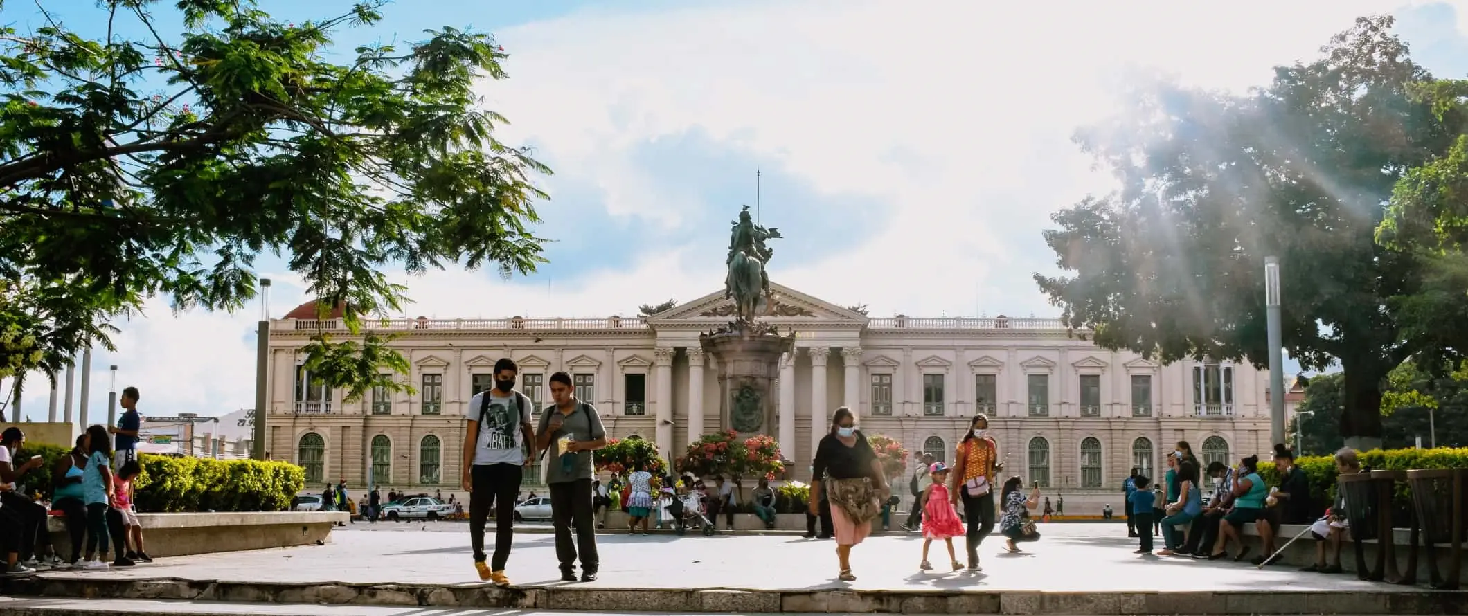 Mensen lopen rond op een plein met een historisch gebouw op de achtergrond in San Salvador, de hoofdstad van El Salvador