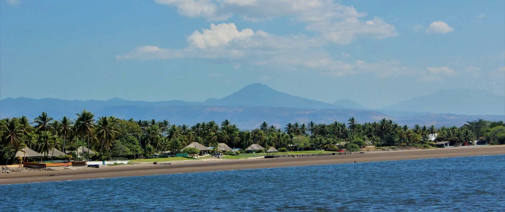 Uitzicht op hutten langs het strand met een vulkaan op de achtergrond in El Salvador