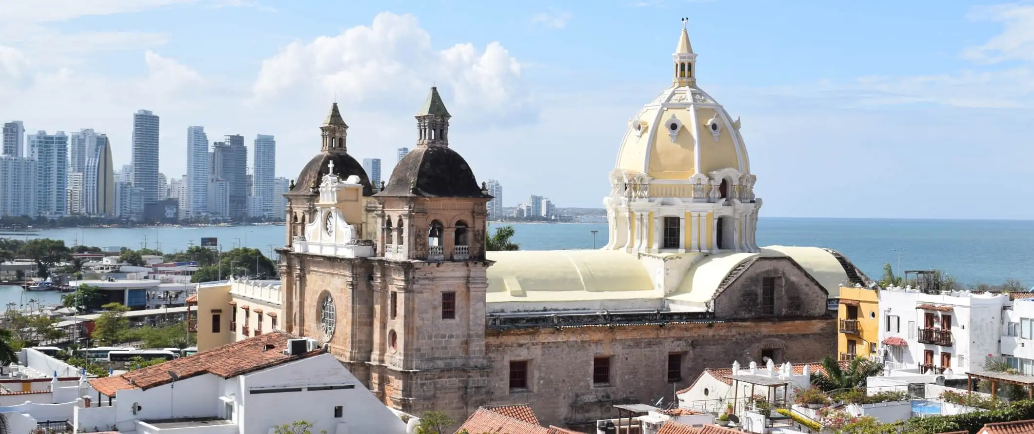 Udsigt over den befæstede by Cartagena, Colombia, med en stor historisk kuppelkirke i forgrunden og moderne skyskrabere i baggrunden