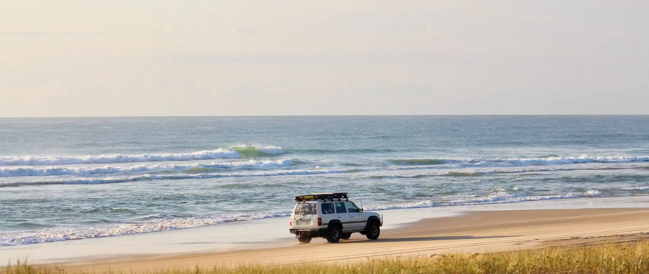 Et enkelt 4WD-kjøretøy på vei nedover den brede sandstranden på Fraser Island, Australia