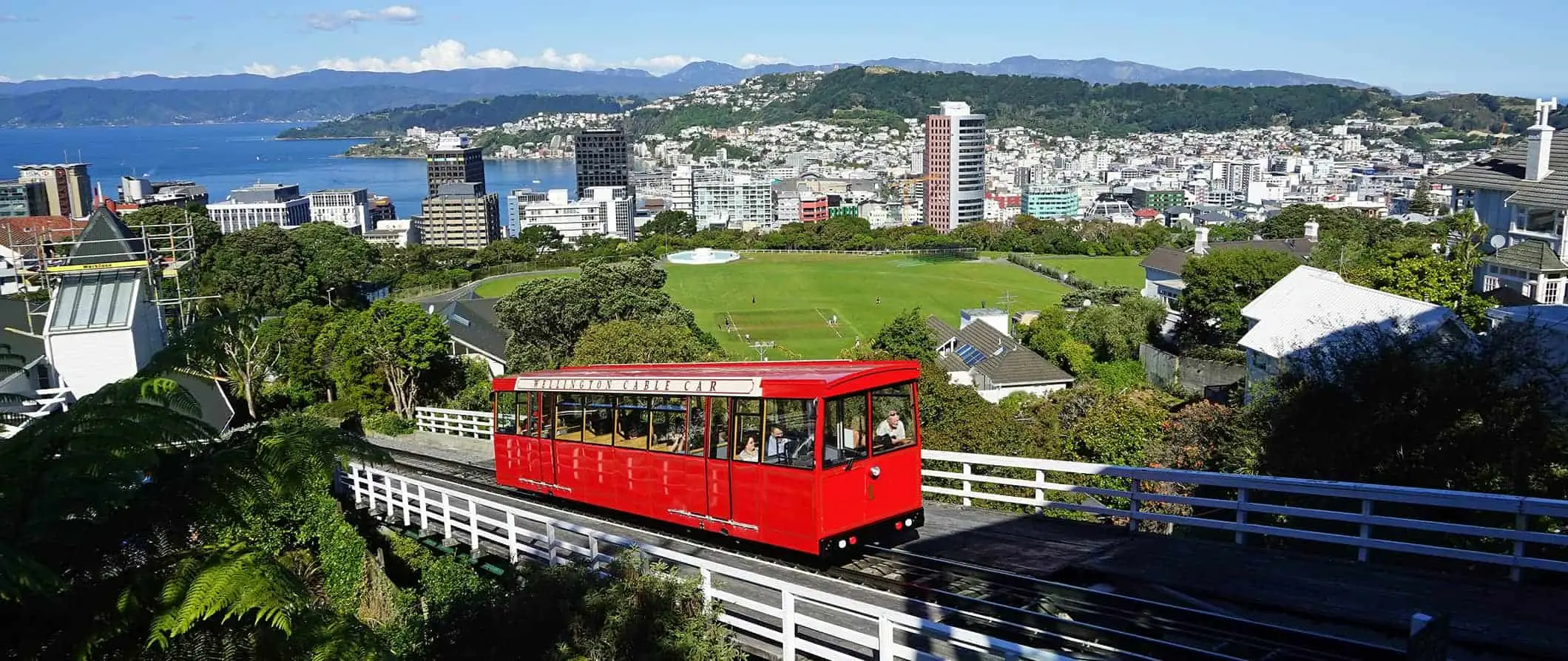 Kereta gantung Wellington merah mendaki lereng bukit dengan latar belakang kota Wellington, Selandia Baru.