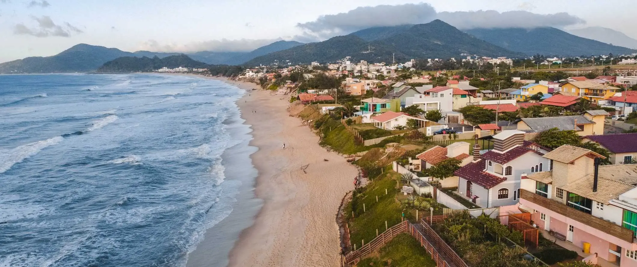 Case colorate de-a lungul plajei cu munți în fundal în Florianópolis, Brazilia