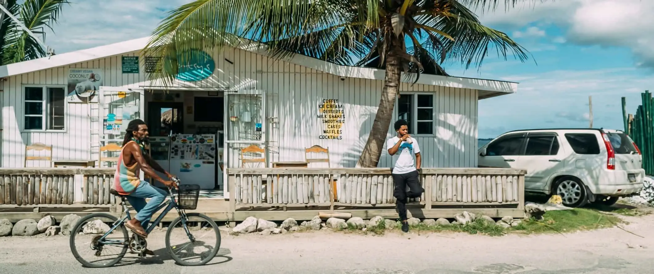 Man fietst door de straat voor een witte bungalow in Jamaica