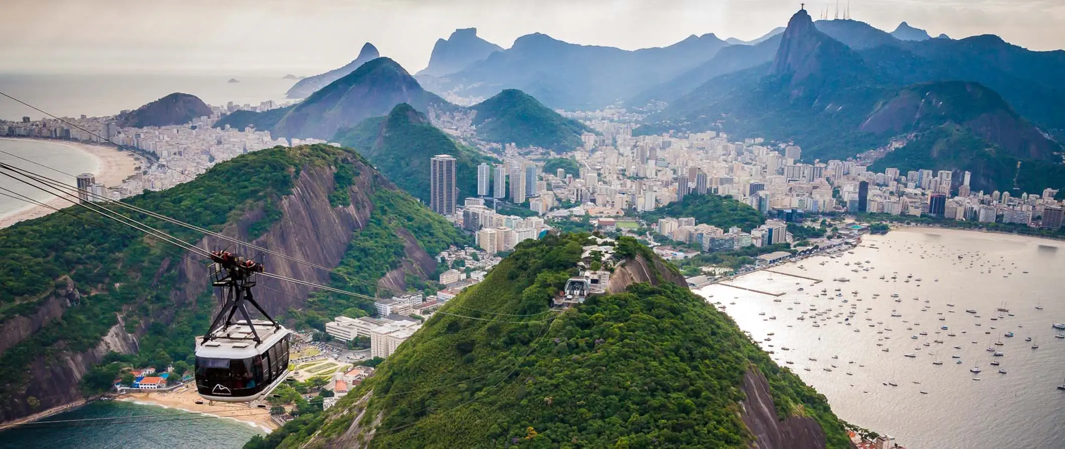 Der Blick auf Rio de Janeiro vom Zuckerhut aus mit grünen Bergen im Hintergrund und einer Seilbahn im Vordergrund