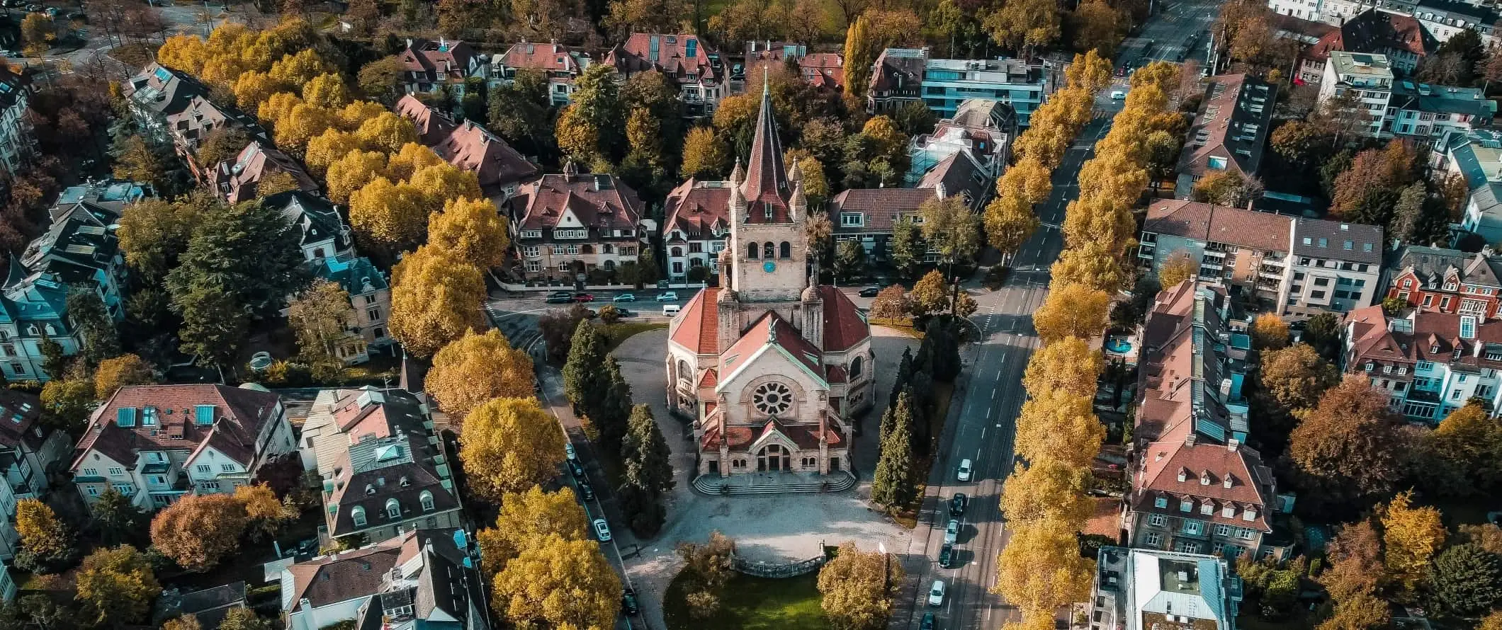 Flygfoto över trädkantade gator med en historisk kyrka på ett torg i Basel, Schweiz