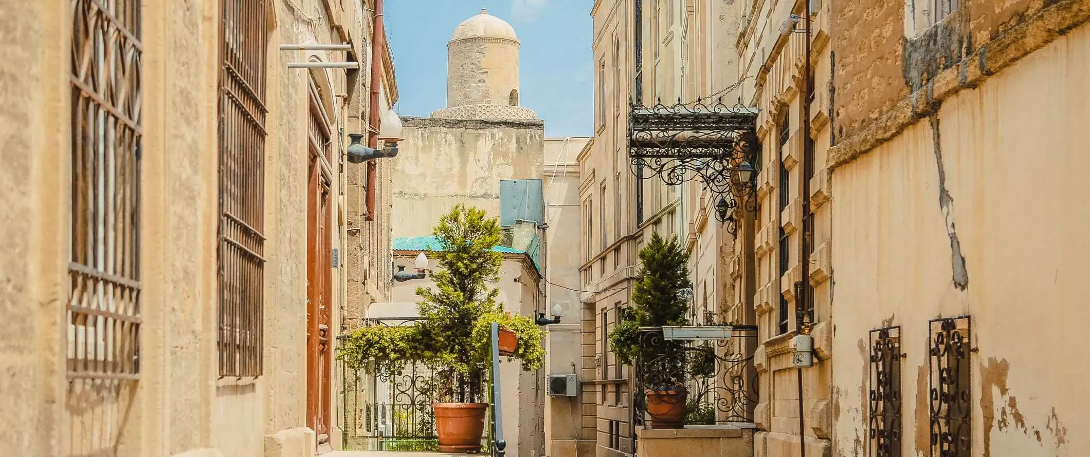 Gadebillede med historiske beige bygninger og et kuppelformet tårn i baggrunden på en lys solskinsdag i Baku, Aserbajdsjan