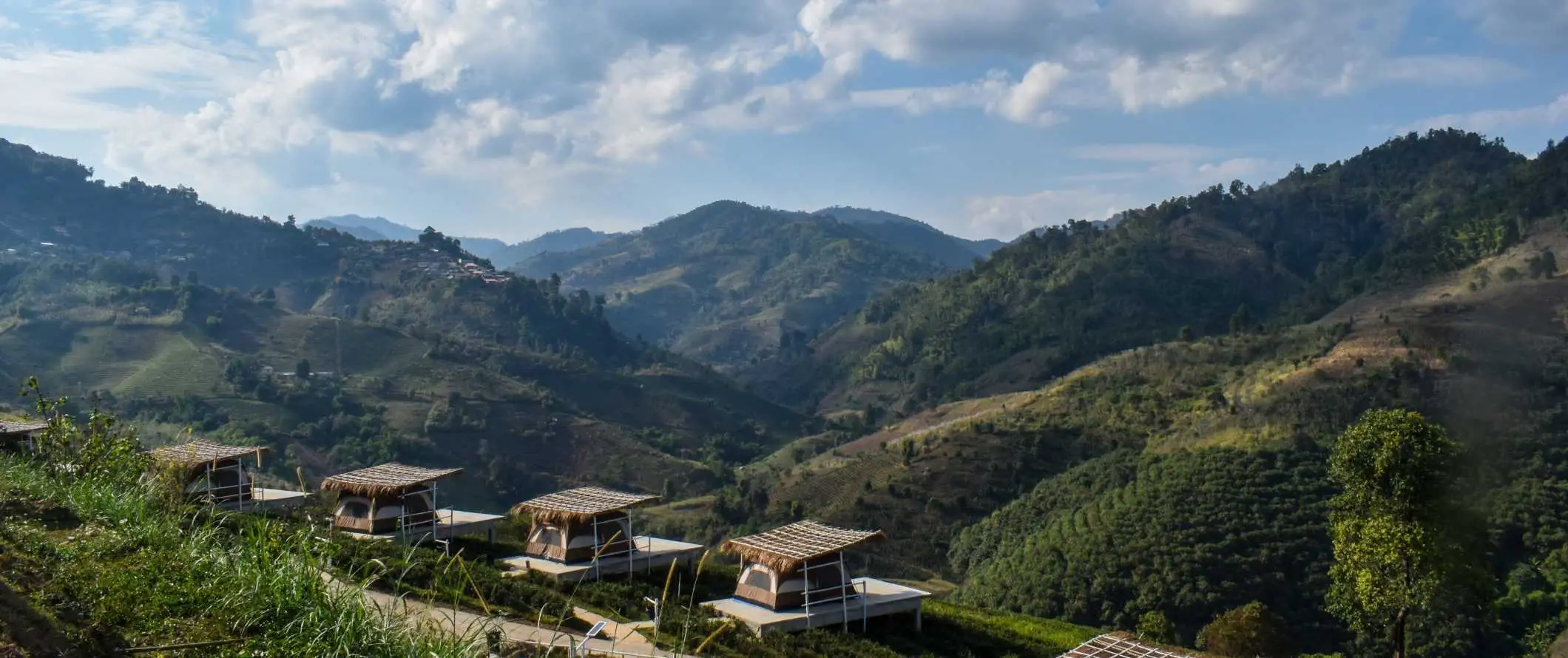 Khemah di atas pelantar di latar depan dengan bukit-bukit hijau di latar belakang di Utara Thailand