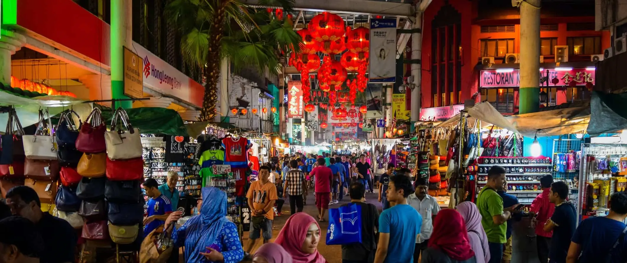 Menschen, die nachts in Kuala Lumpur, Malaysia, eine überfüllte Fußgängerzone entlang gehen, die von Geschäften gesäumt ist