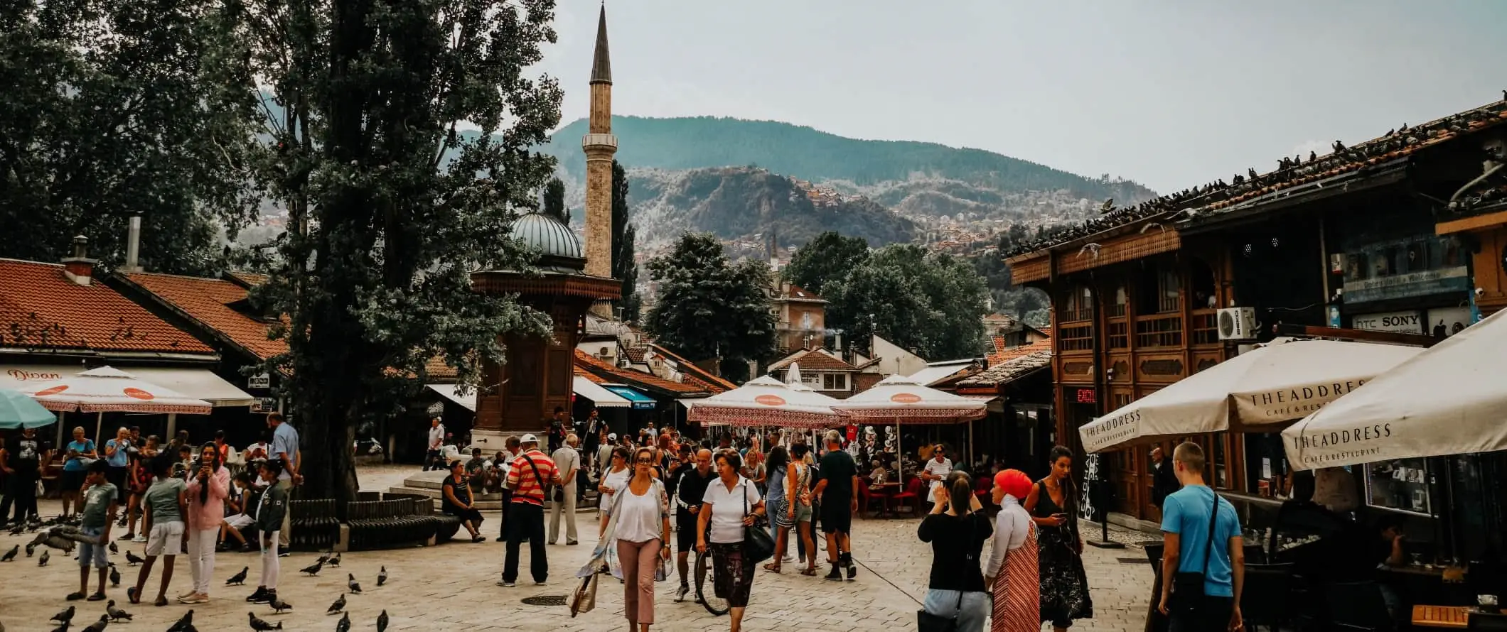 Historisk torg fylt med duer og mennesker og en minaret i bakgrunnen i Sarajevo, Bosnia og Hercegovina