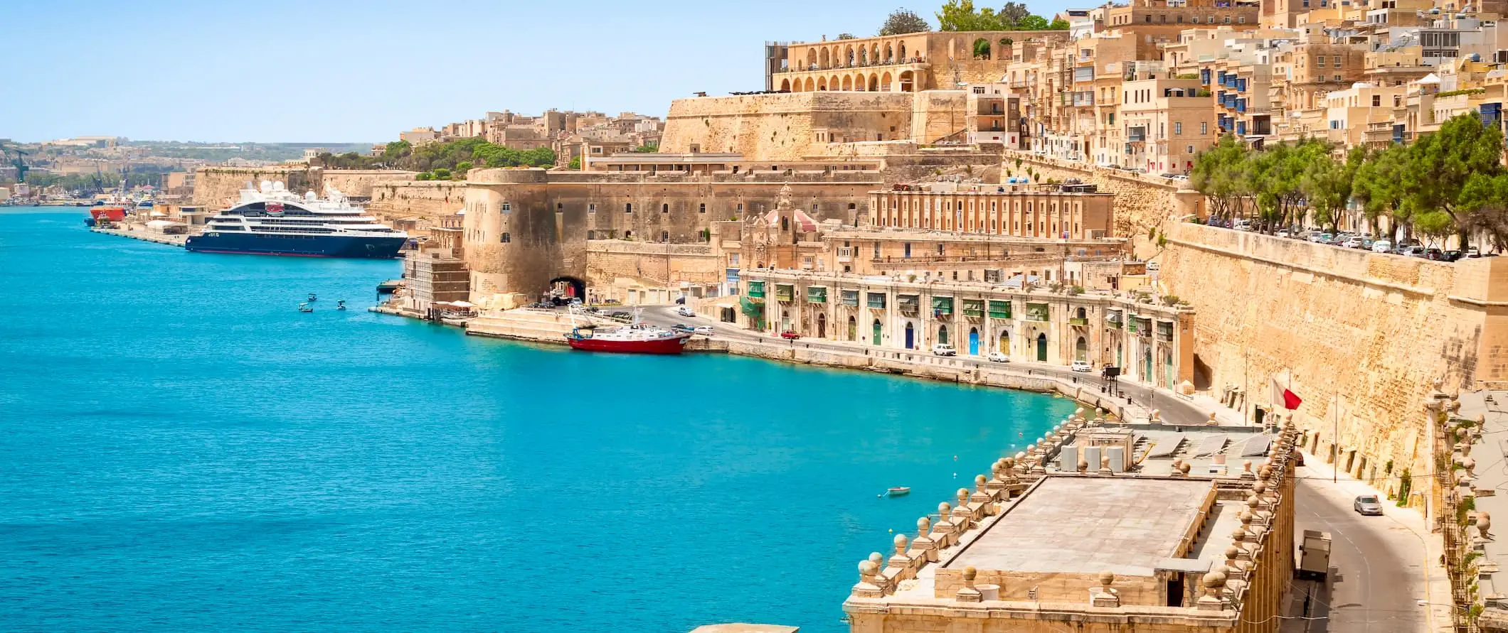 pemandangan pantai di Malta, dibarisi oleh bangunan bersejarah yang menjulang tinggi berhampiran pelabuhan