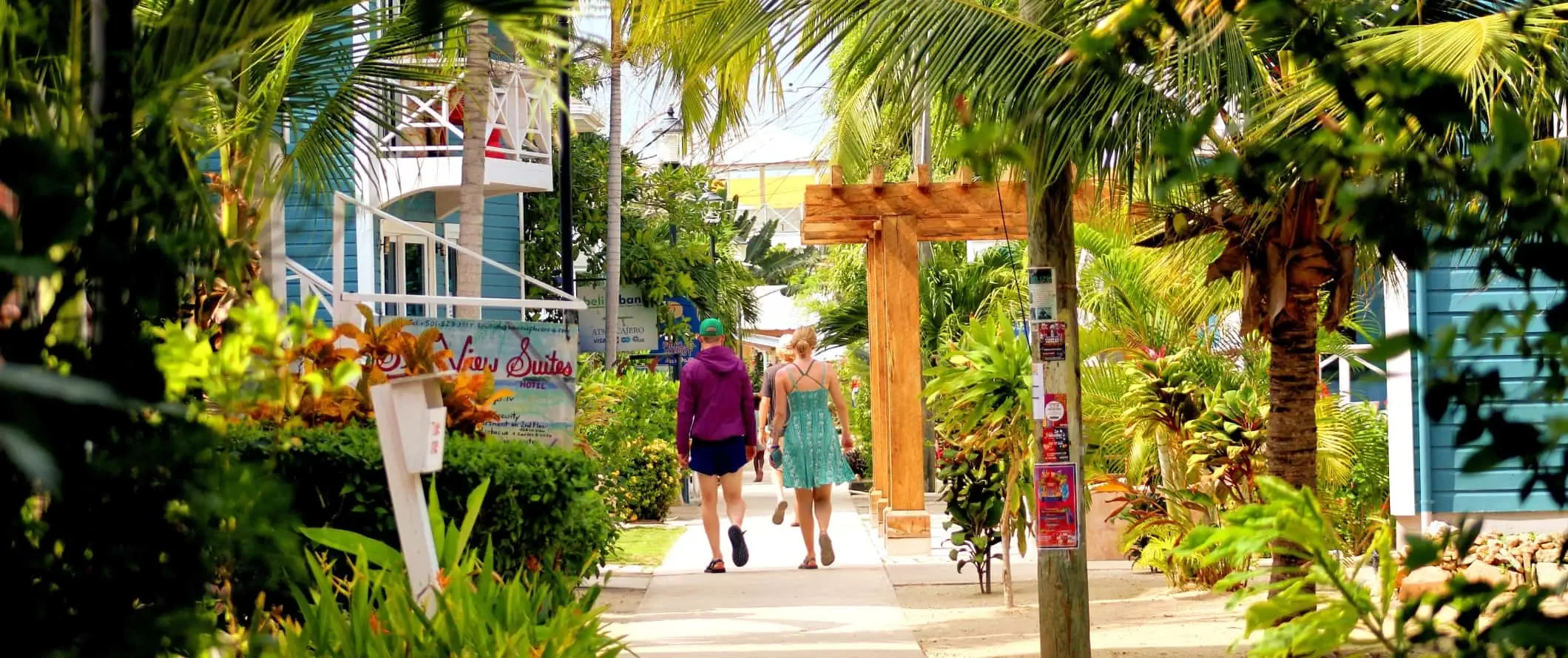 Toeristen lopen over een trottoir vol weelderige palmen in Placencia, Belize