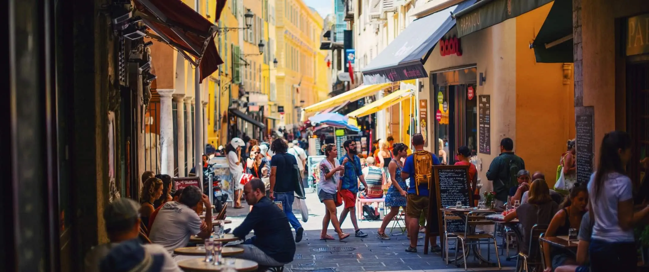 Jalan pejalan kaki yang sibuk dipenuhi orang-orang yang berjalan-jalan dan duduk di kafe luar ruangan di kota tua di Nice, Prancis