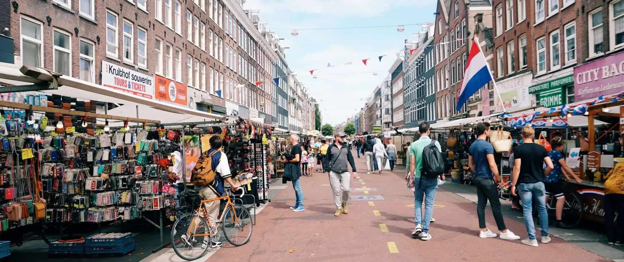 Ľudia kráčajúci po pešej ulici lemovanej trhovými stánkami v holandskom Amsterdame.