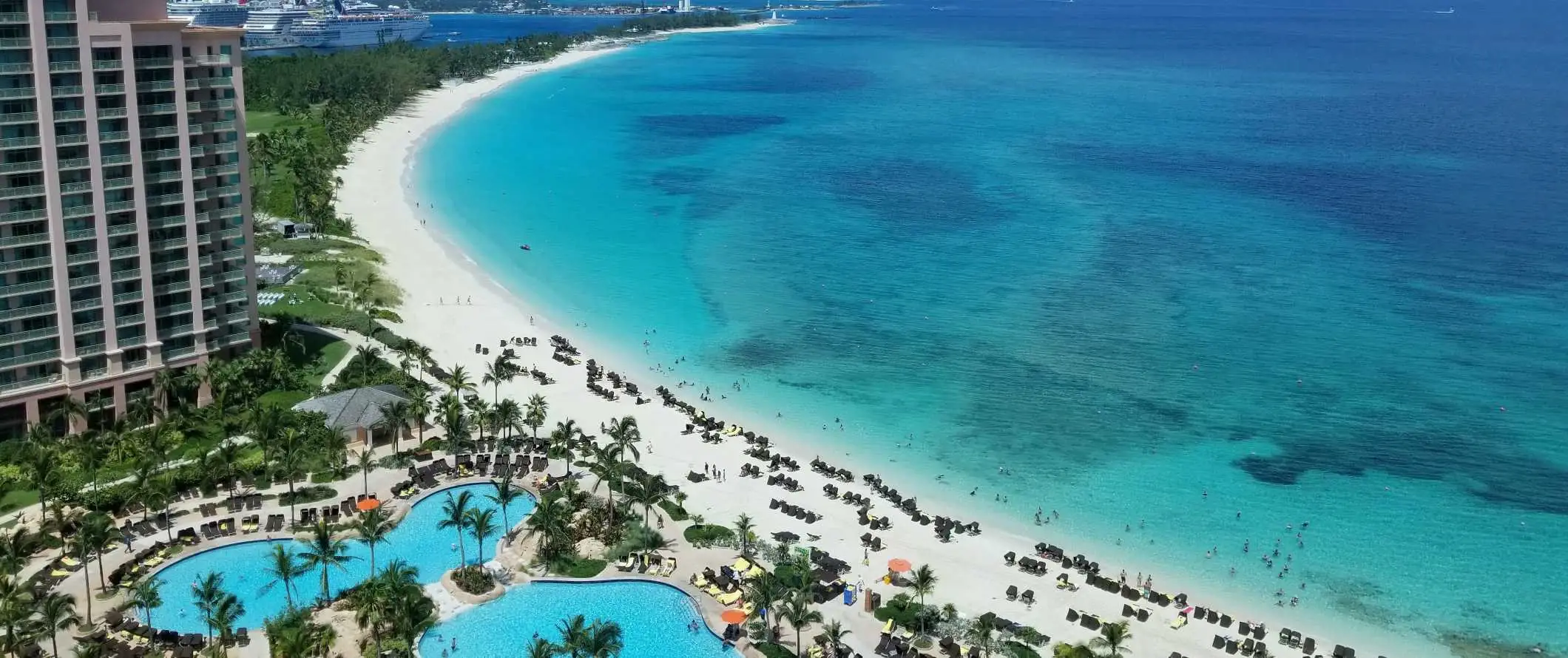 Droneudsigt over resortets pools på et stort hotel langs stranden med krystalklart turkisblåt vand på Bahamas