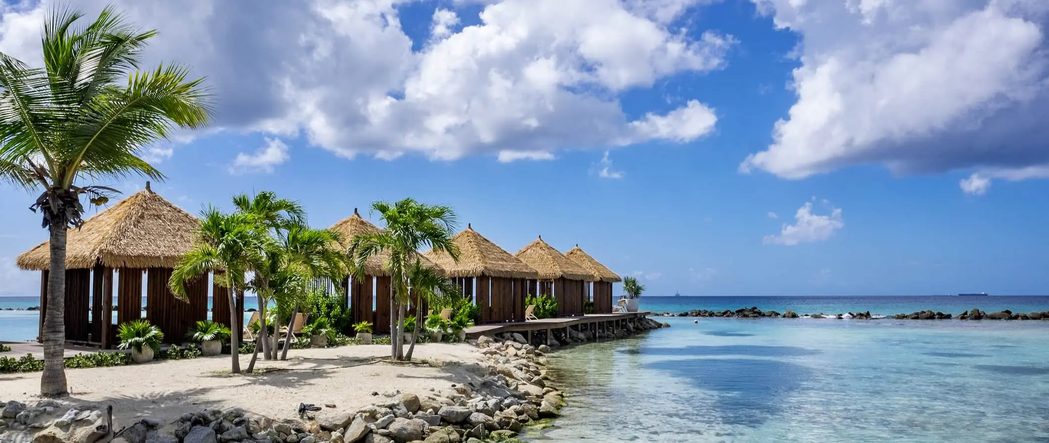 Avslappende strandbungalower og skyggefulle lenestoler på den solfylte kysten av Aruba i Karibia