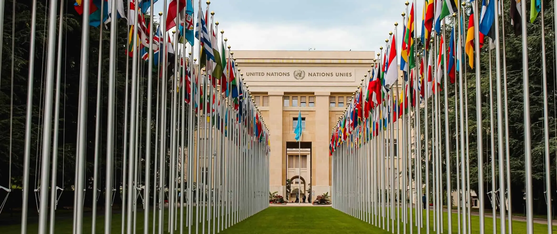 Edificio de las Naciones Unidas con dos filas de banderas de todo el mundo al frente, en Ginebra, Suiza