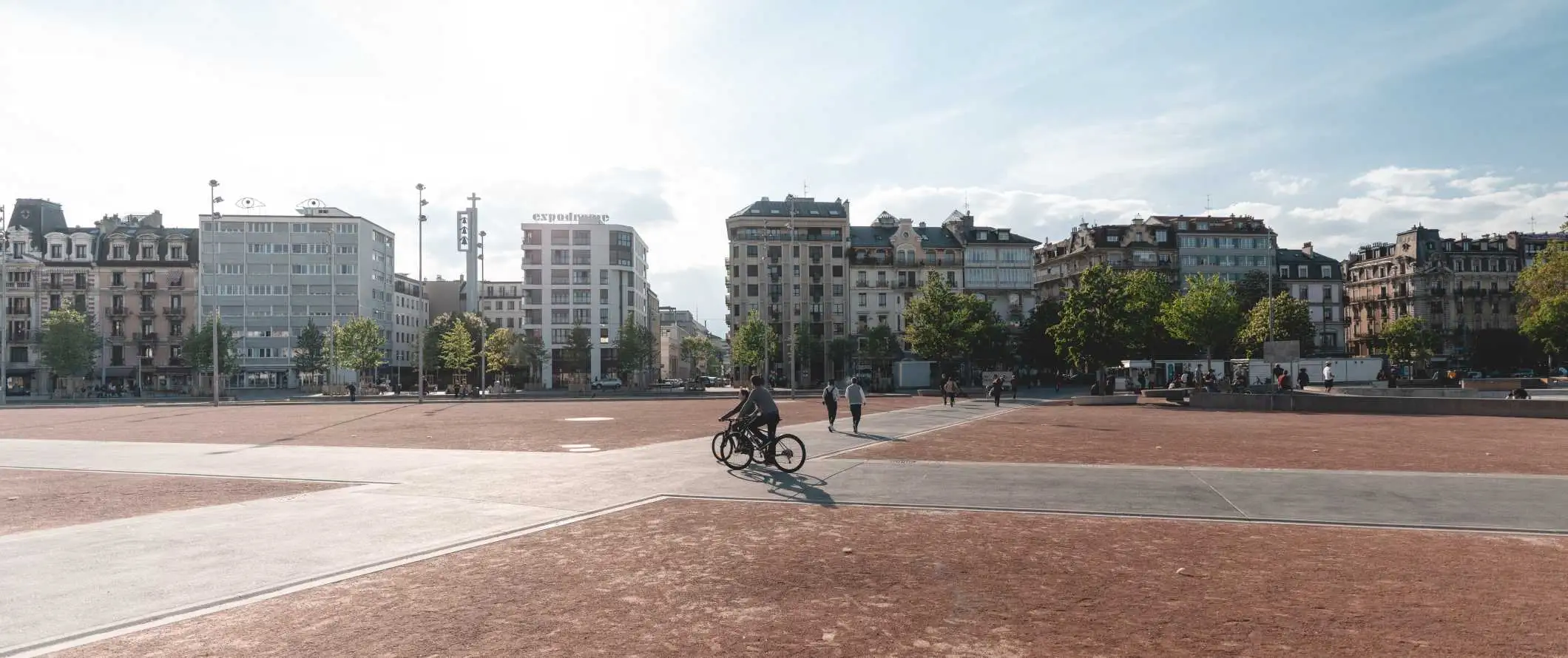 Persone che camminano e vanno in bicicletta attraverso una grande piazza a Ginevra, in Svizzera