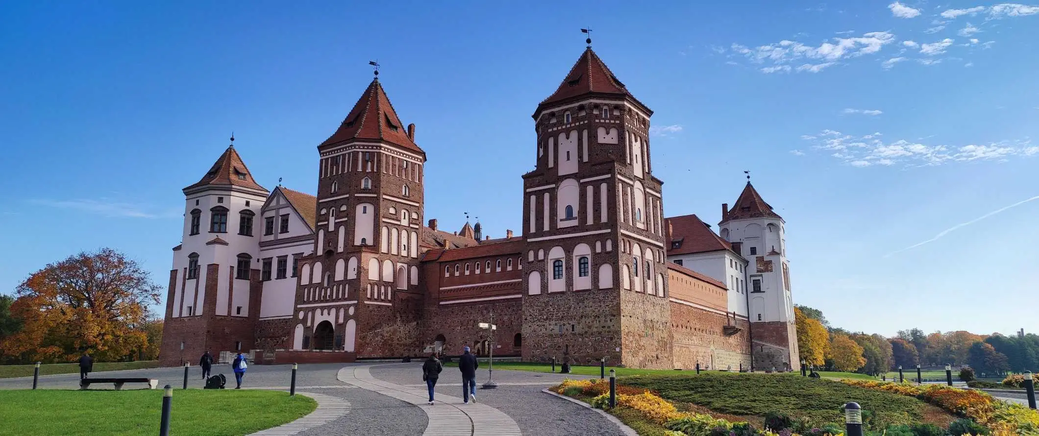 Belarus'ta kırmızı tuğlalı görkemli bir kale olan Mir Kalesi'ne giden eğimli bir yolda yürüyen insanlar