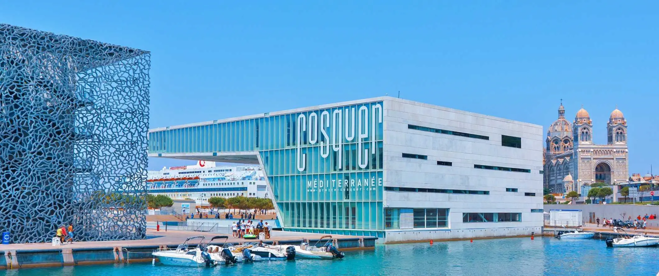 Dumaong ang mga motorboat sa harap ng mga futuristic na gusali at isang malaking cruise ship na nakaharap sa background sa Marseille, France