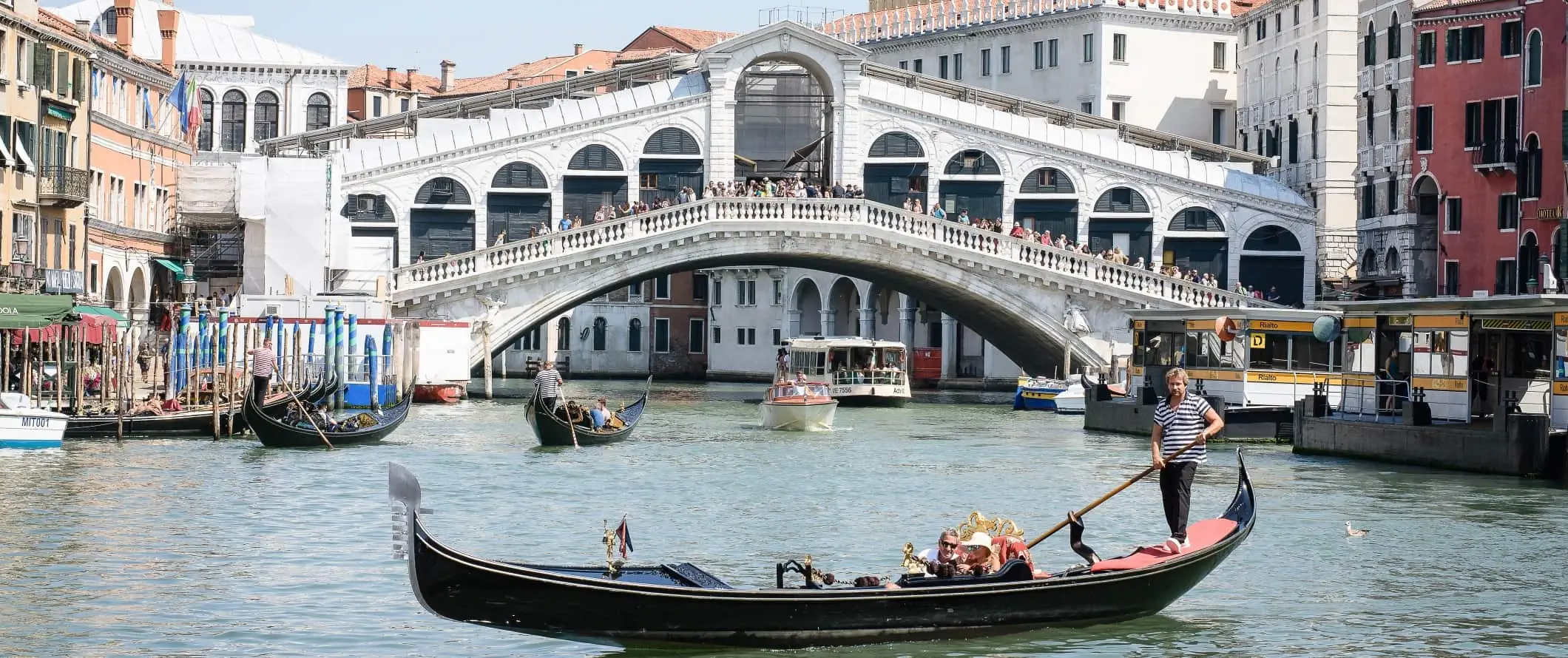 Vista dello storico ponte di Rialto con un uomo che guida una gondola di fronte, a Venezia, Italia.