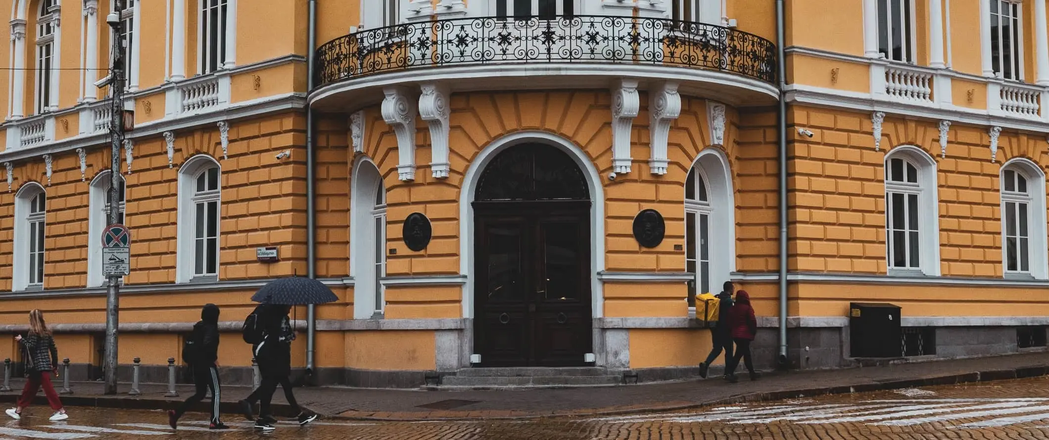 Menschen, die im Regen die Straße entlang gehen, vorbei an einem leuchtend gelben Gebäude in Sofia, Bulgarien