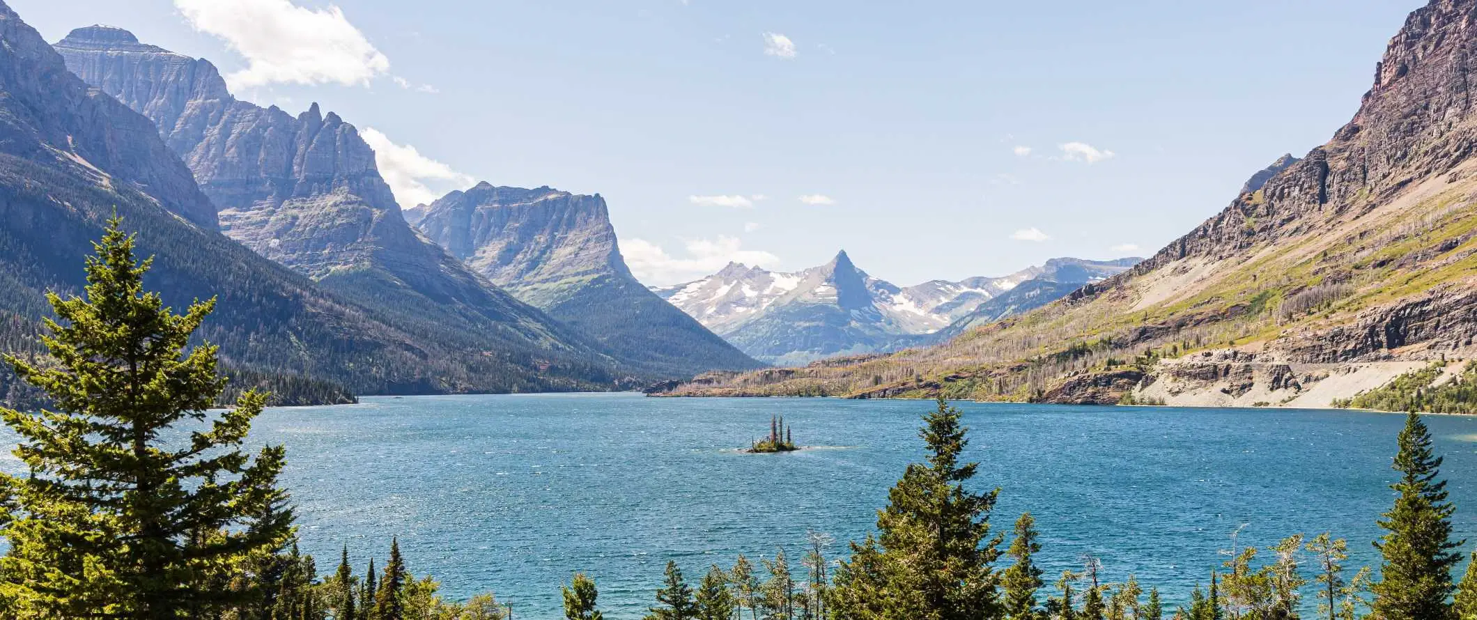 Dramatische, grillige bergen voor een uitgestrekt blauw meer met een klein, met bomen bedekt eiland in het midden, in Glacier National Park, Verenigde Staten.