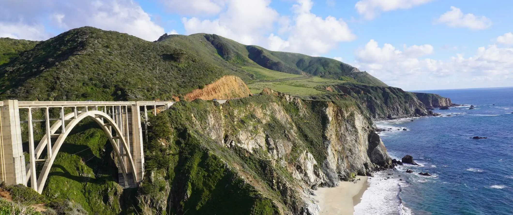 미국 캘리포니아주에 있는 무성한 언덕을 배경으로 퍼시픽 코스트 하이웨이(Pacific Coast Highway)를 따라 있는 아치형 빅스비 크릭 브리지(Bixby Creek Bridge)입니다.