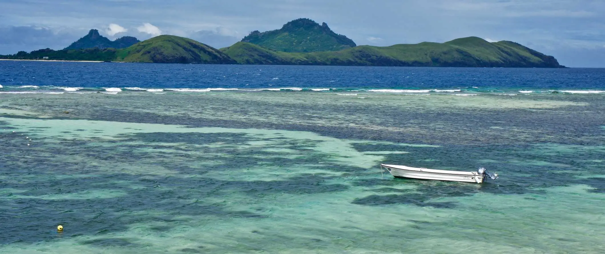 Ein kleines Boot, das in den tropischen Gewässern vor der Küste einer Insel in Fidschi vor Anker liegt