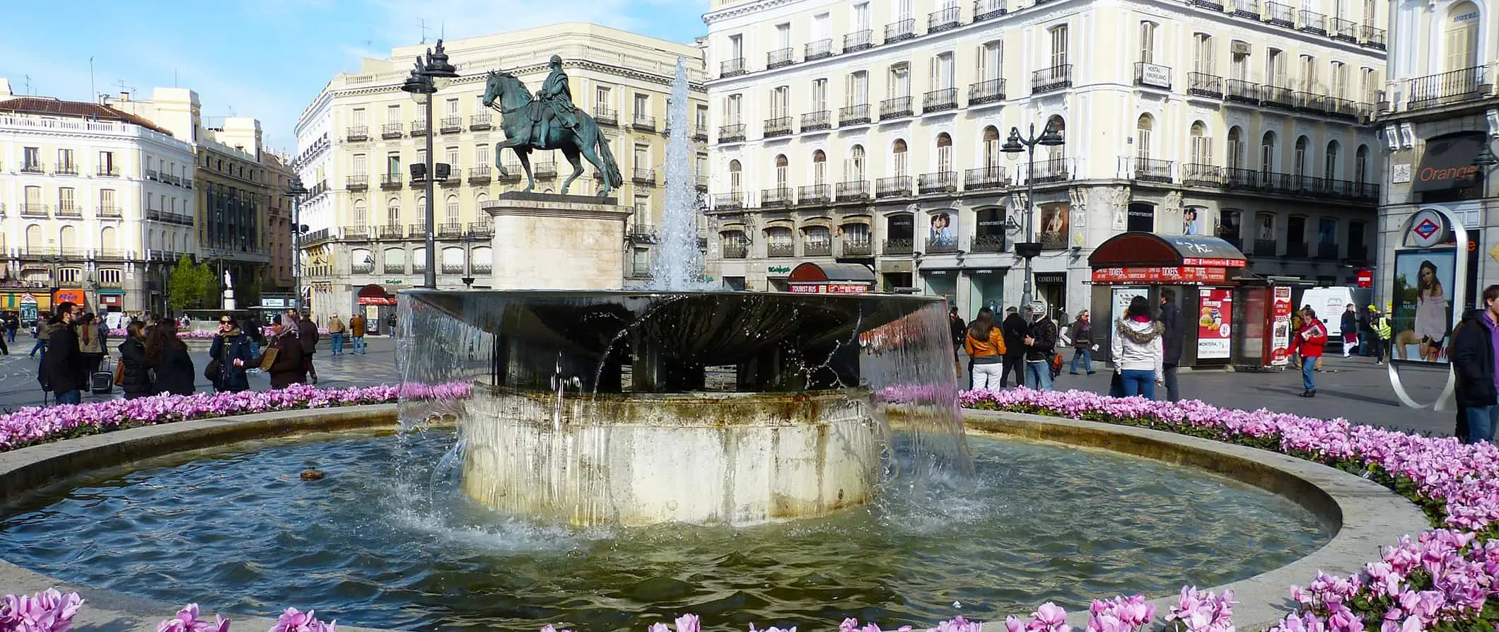 Madrid, İspanya'da güneşli bir günde büyük, tarihi bir çeşmenin etrafında dolaşan insanlar