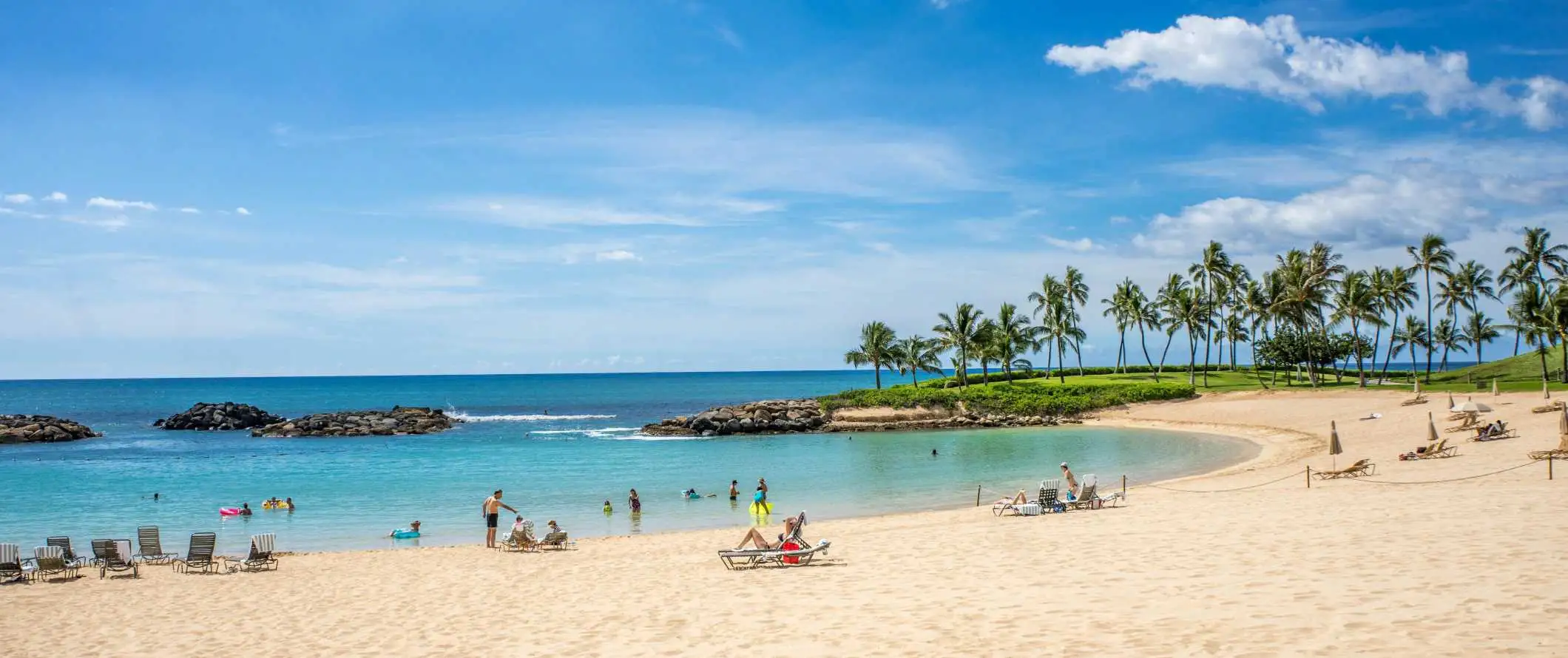 Emberek heverésznek a tengerparton, pálmafákkal a háttérben Hawaii-on.