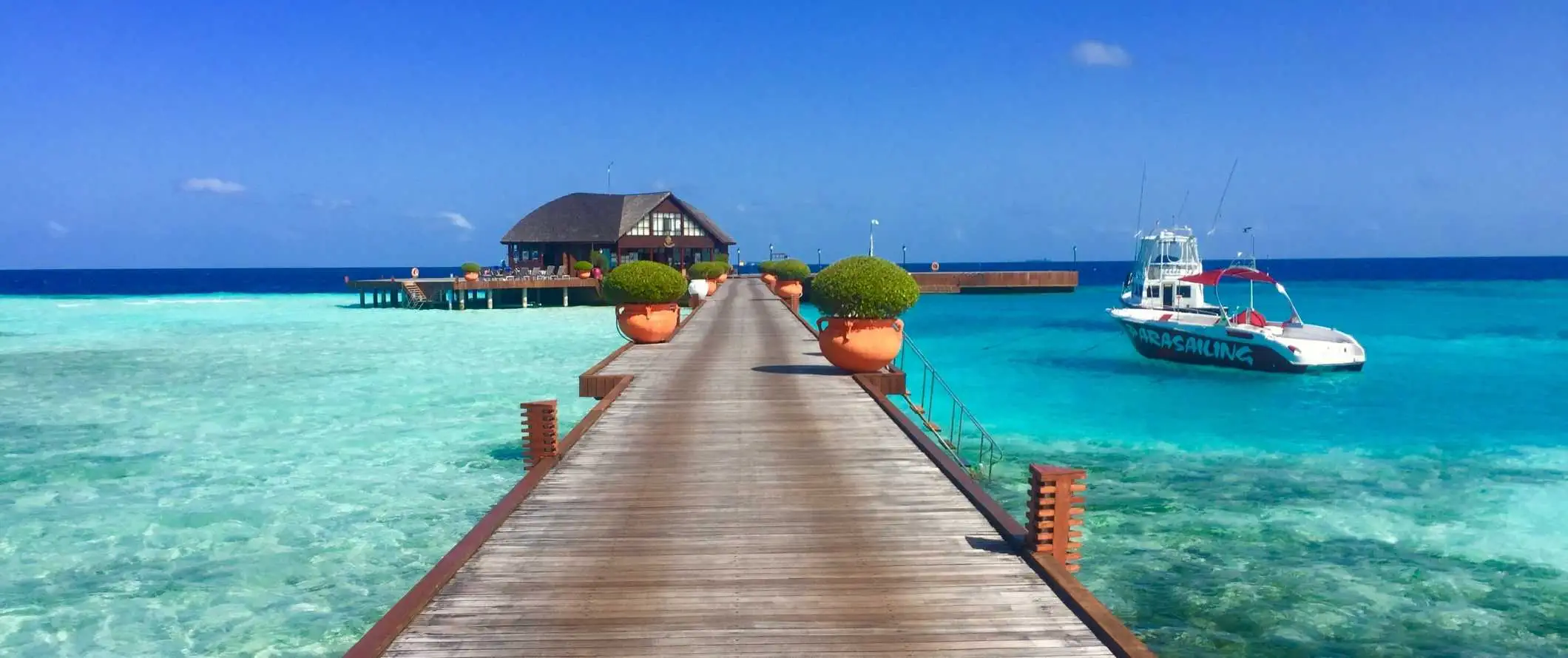 Mga bangka na naka-angkla sa isang pantalan na may malaking bungalow sa ibabaw ng tubig sa Maldives