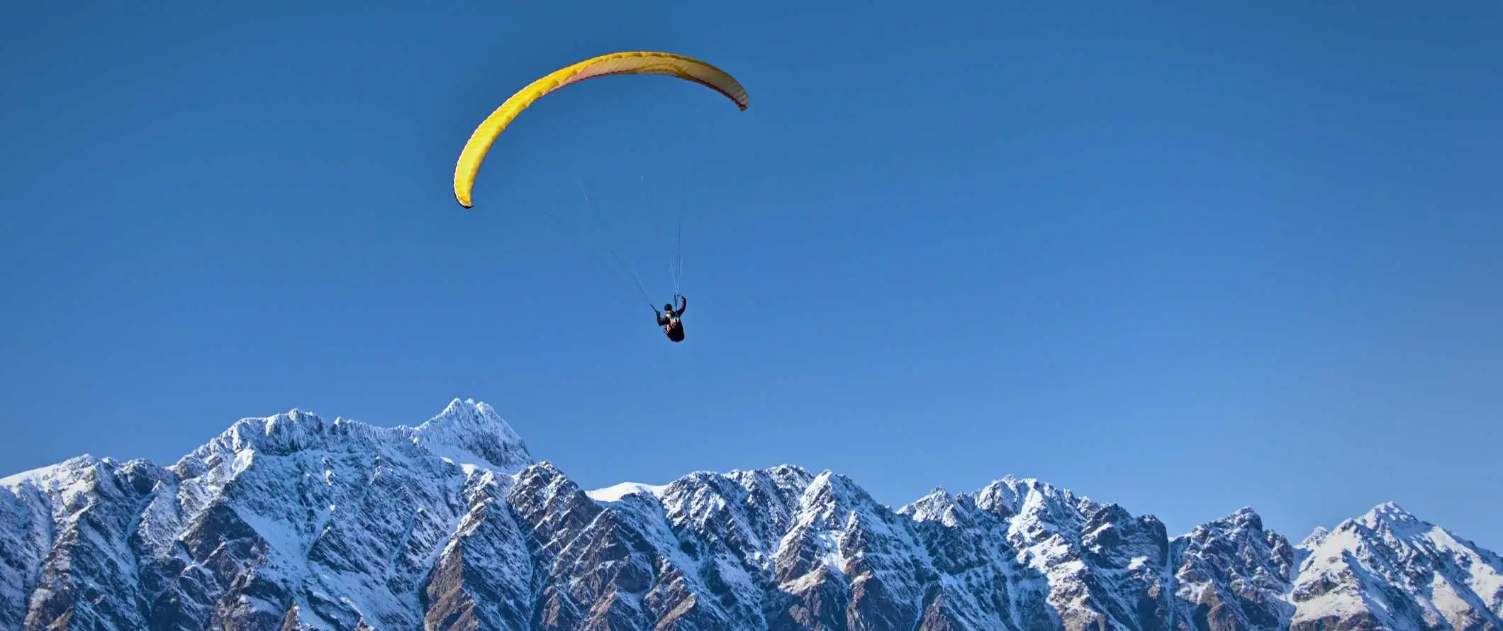 Iemand parachuteert over besneeuwde bergtoppen in Nieuw-Zeeland.