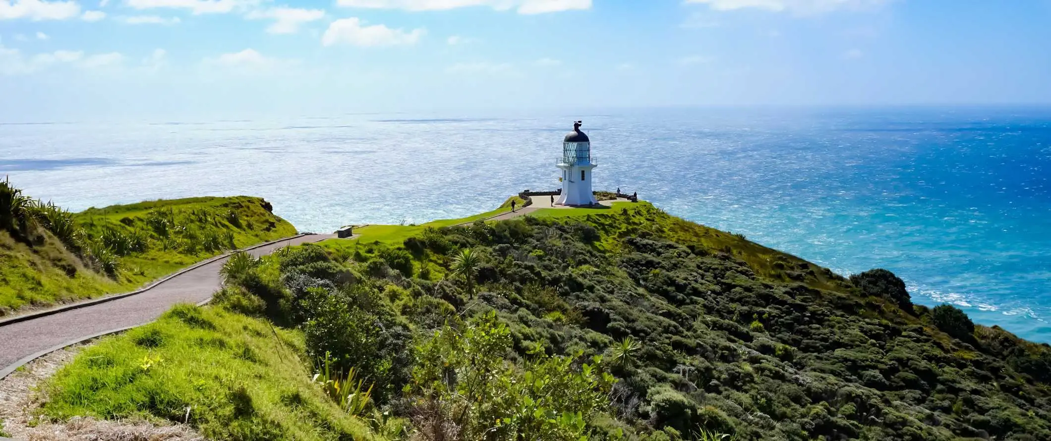 Faro bianco a cupola sul bordo di una lussureggiante scogliera verde con il mare sullo sfondo nella Baia delle Isole, Nuova Zelanda