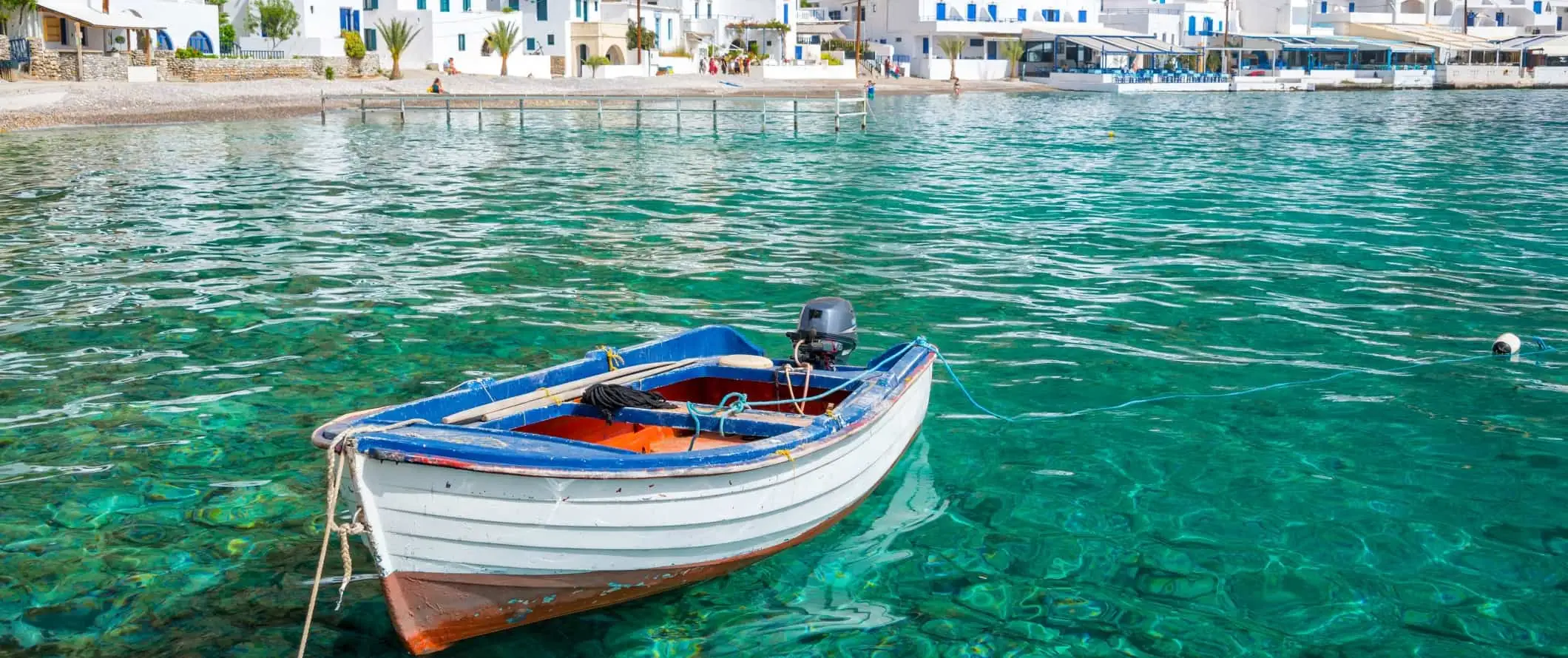 Nag-iisang bangka sa malinaw na turkesa na tubig ng isang bay na may linyang puting bahay sa isla ng Crete sa Greece.