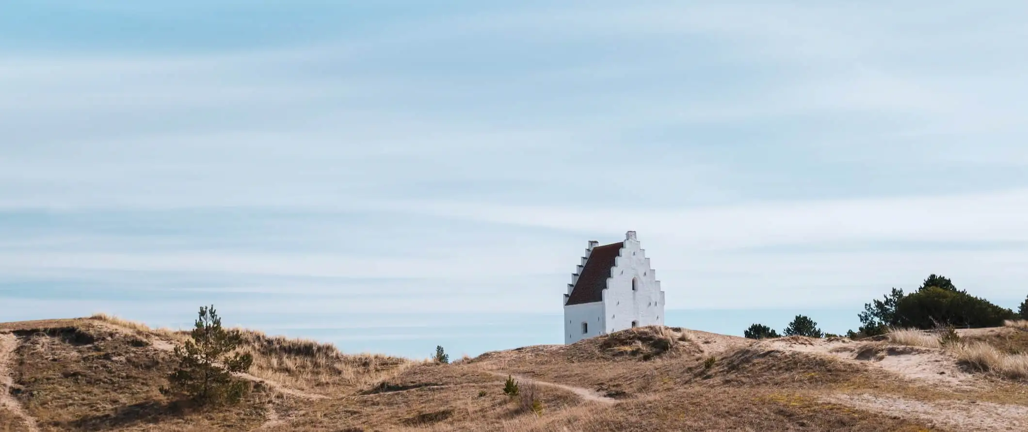 Uma pequena igreja branca na costa acidentada e soprada pelo vento da Jutlândia, na Dinamarca