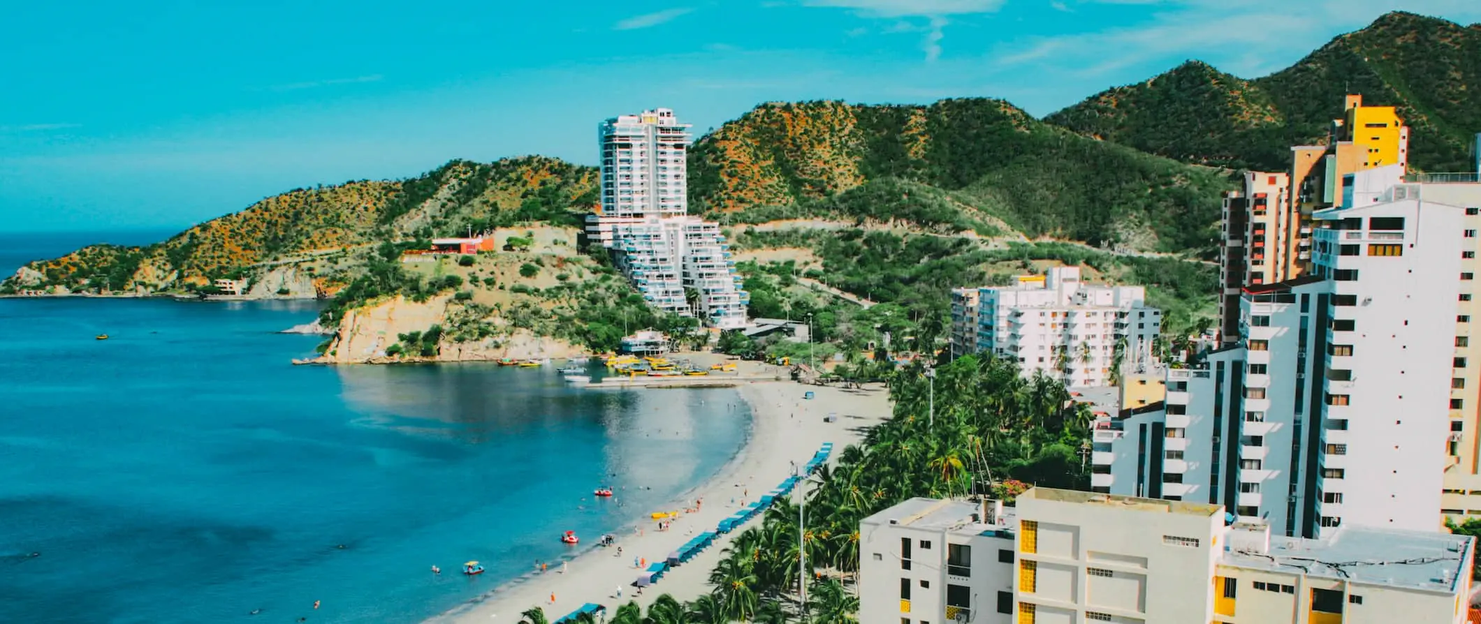 Una vista aérea de la playa de Santa Marta, Colombia, con hoteles a lo largo de la costa y colinas al fondo.