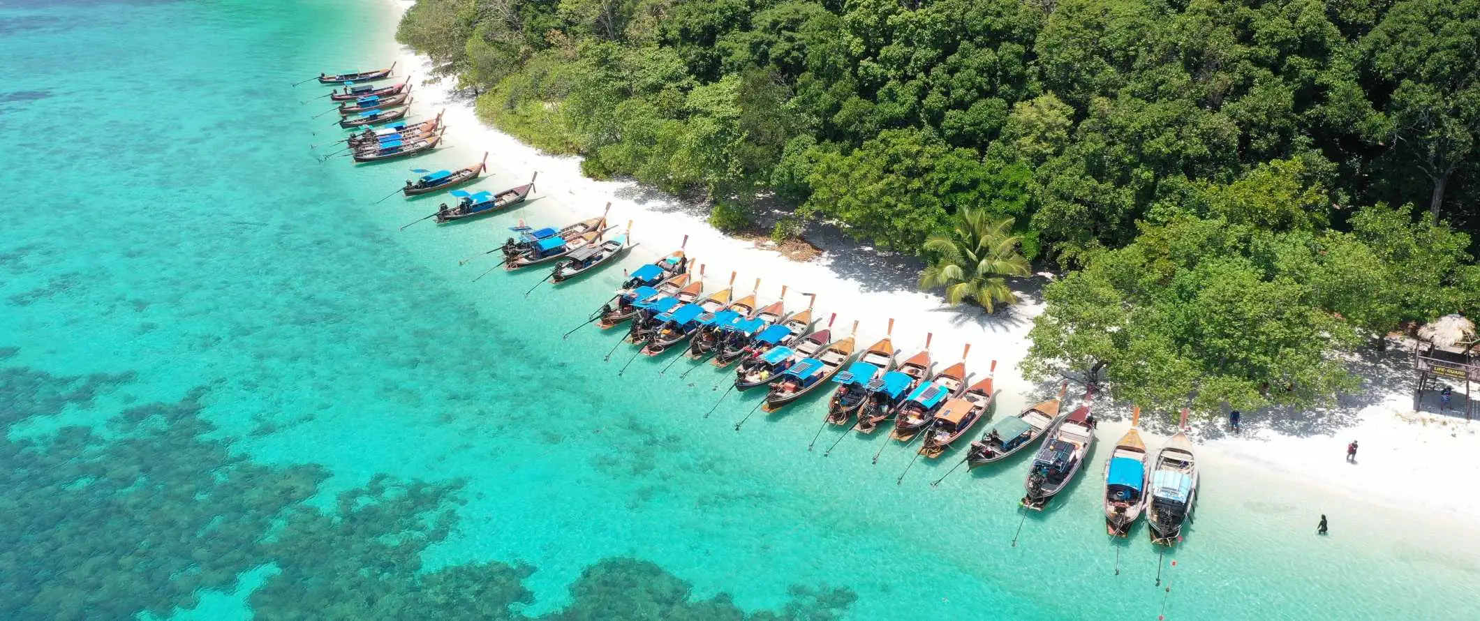 Flygfoto över en rad longtailbåtar som ligger till kaj på en strand på ön Ko Lipe, Thailand